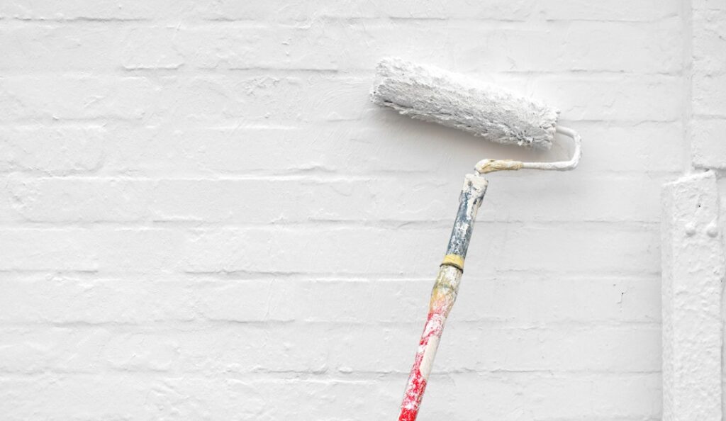 A paint roller is painting the wall white.
